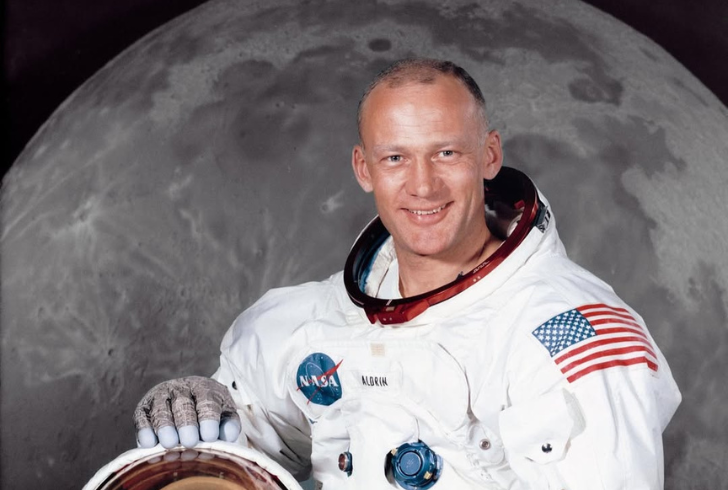 A portrait of Buzz Aldrin in his astronaut suit with the moon in the background